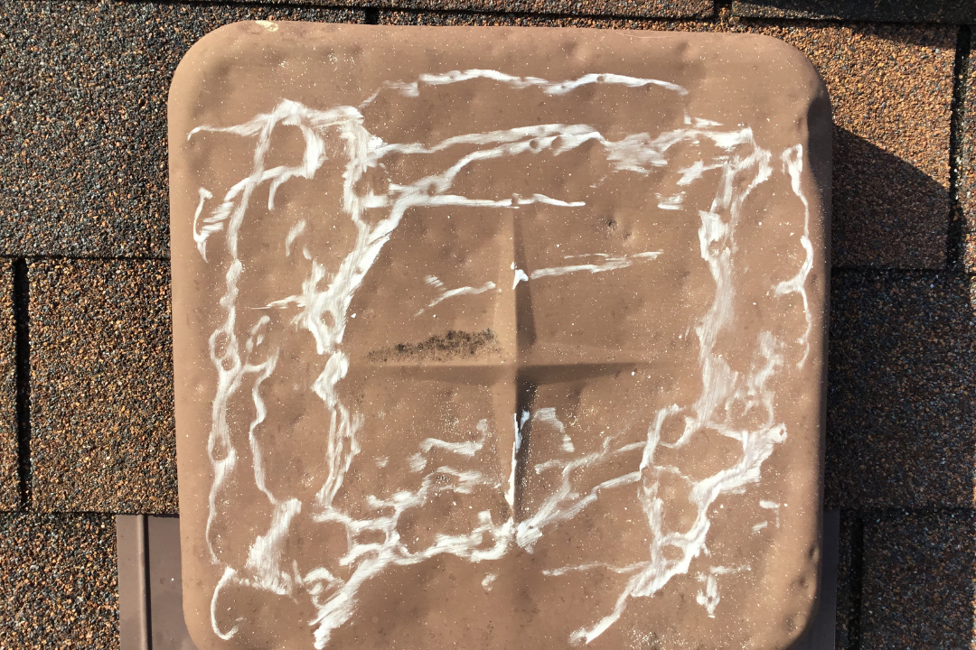 Box vent cap covered in white chalk marks documenting hail hits — dents visible under chalk, shingles on both sides showing granule loss