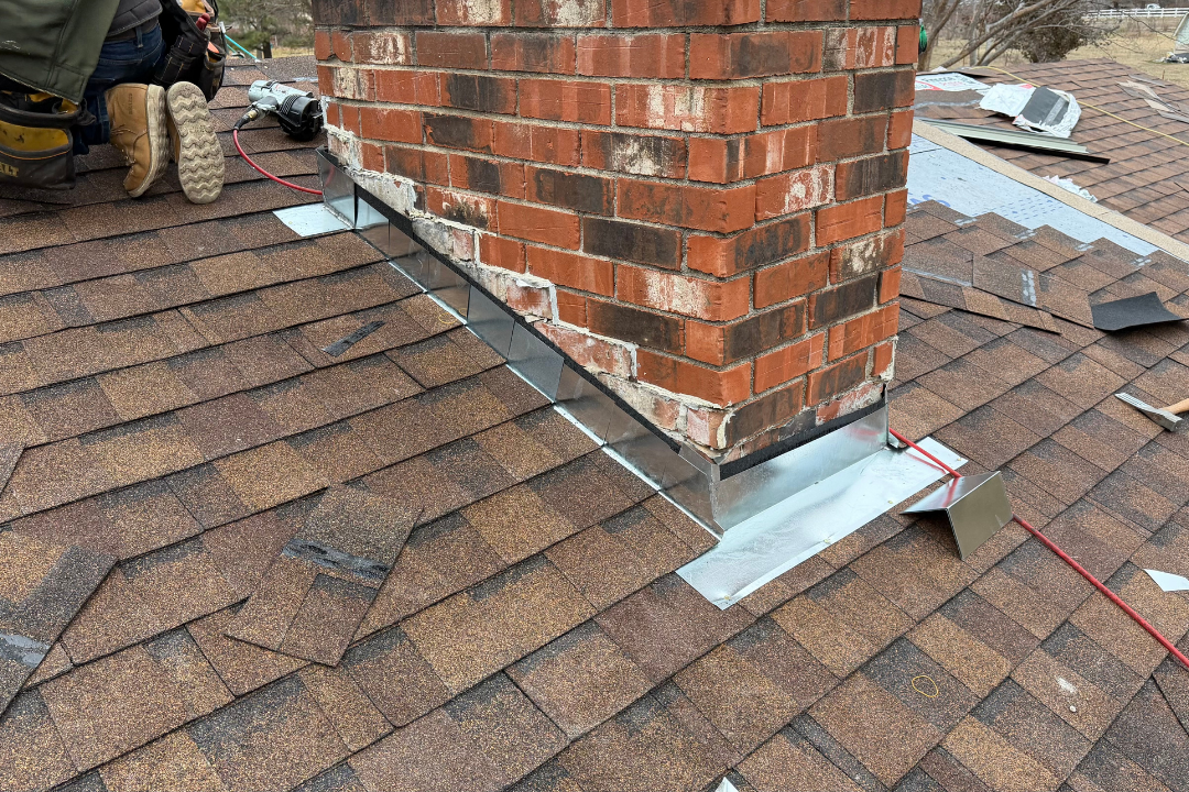 Fresh galvanized chimney flashing install — step and counter flashing wrapping brick chimney, DeWalt nail gun, hammer on roof, crew member's boots visible top left