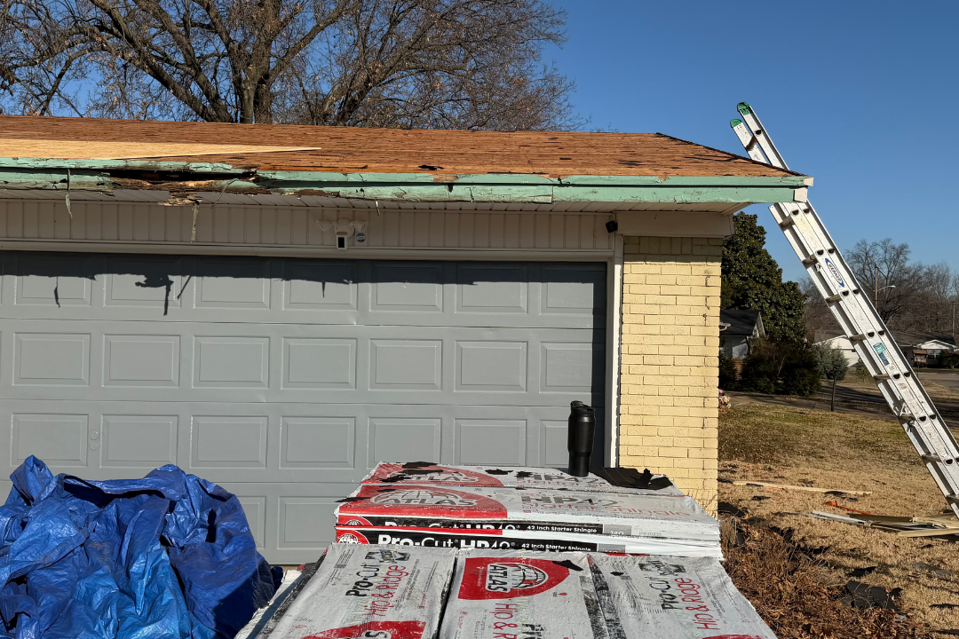 Garage tear-off in progress — old shingles stripped, decking exposed, rotted eave edge visible, Atlas Pro-Cut bundles staged in foreground, ladder up, blue sky