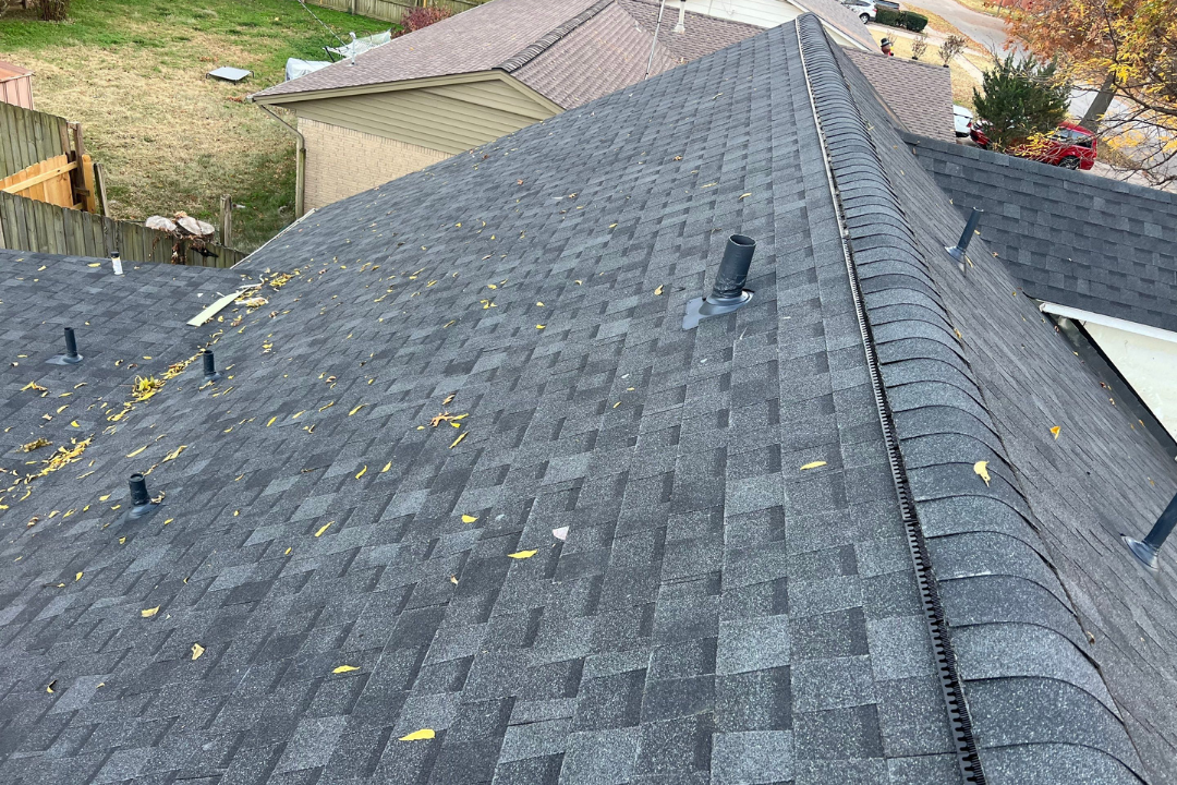 Fresh dark gray shingle roof with continuous ridge vent full length — pipe jacks installed, fall leaves on new shingles, Tulsa neighborhood