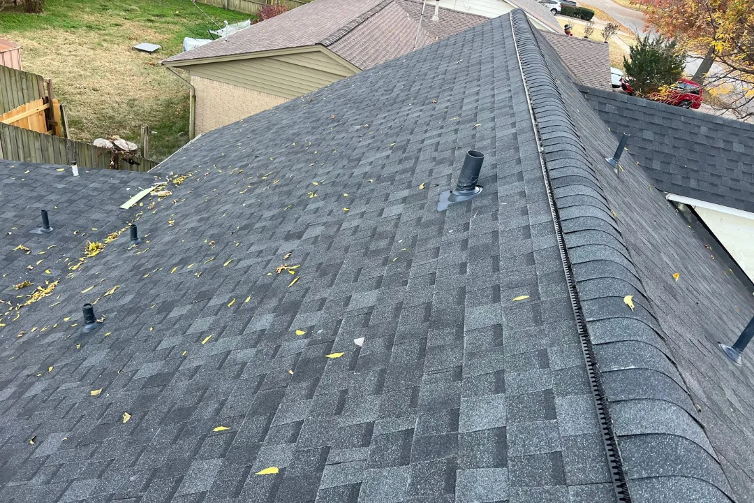 Fresh dark gray shingle roof with continuous ridge vent full length — pipe jacks installed, fall leaves on new shingles, Tulsa neighborhood