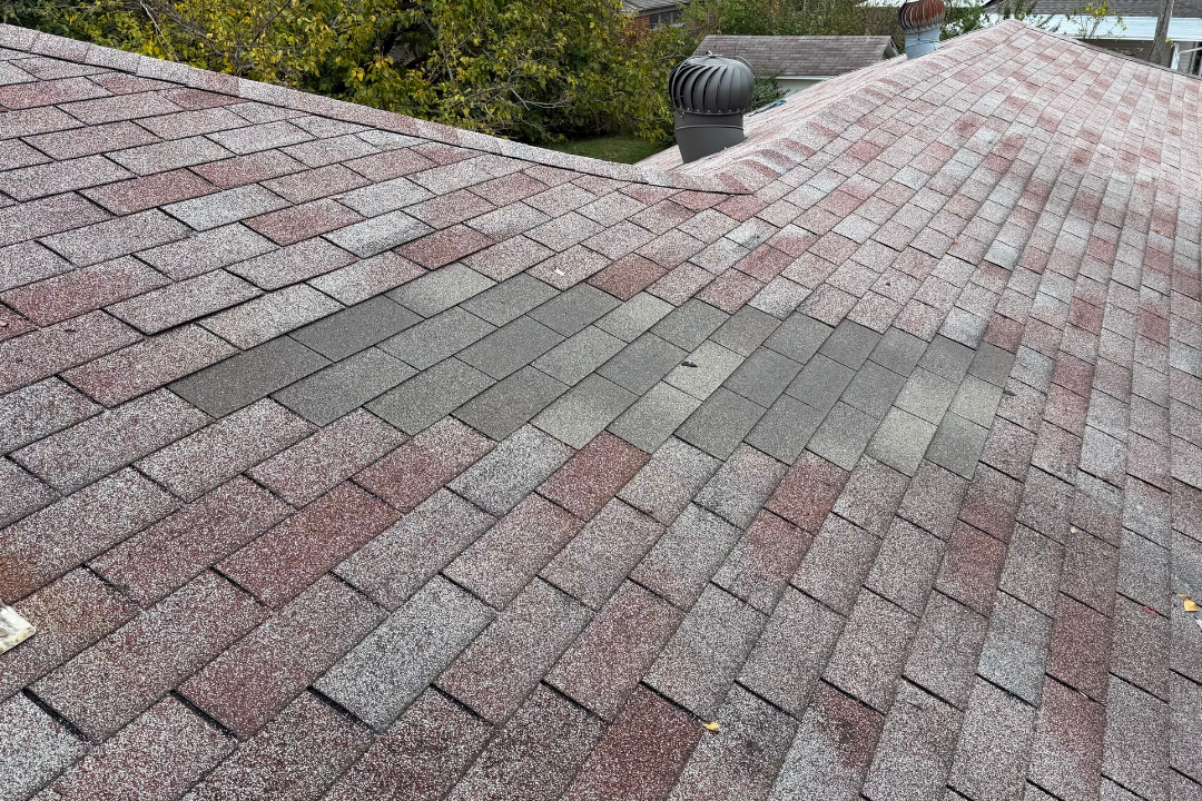 Completed shingle repair patch — gray replacement shingles in older red/brown roof, honest color mismatch visible, turbine vent background