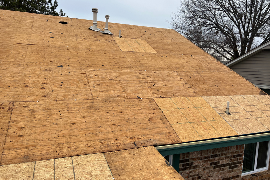 Partial OSB replacement on old plywood — color contrast between old/new decking, pipe jacks roughed in, brick home