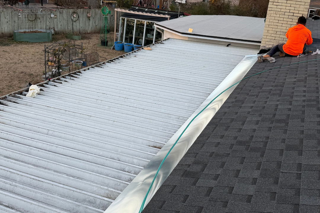 Crew member in orange hoodie working metal-to-shingle transition — fresh dark shingles, custom flashing, backyard setting