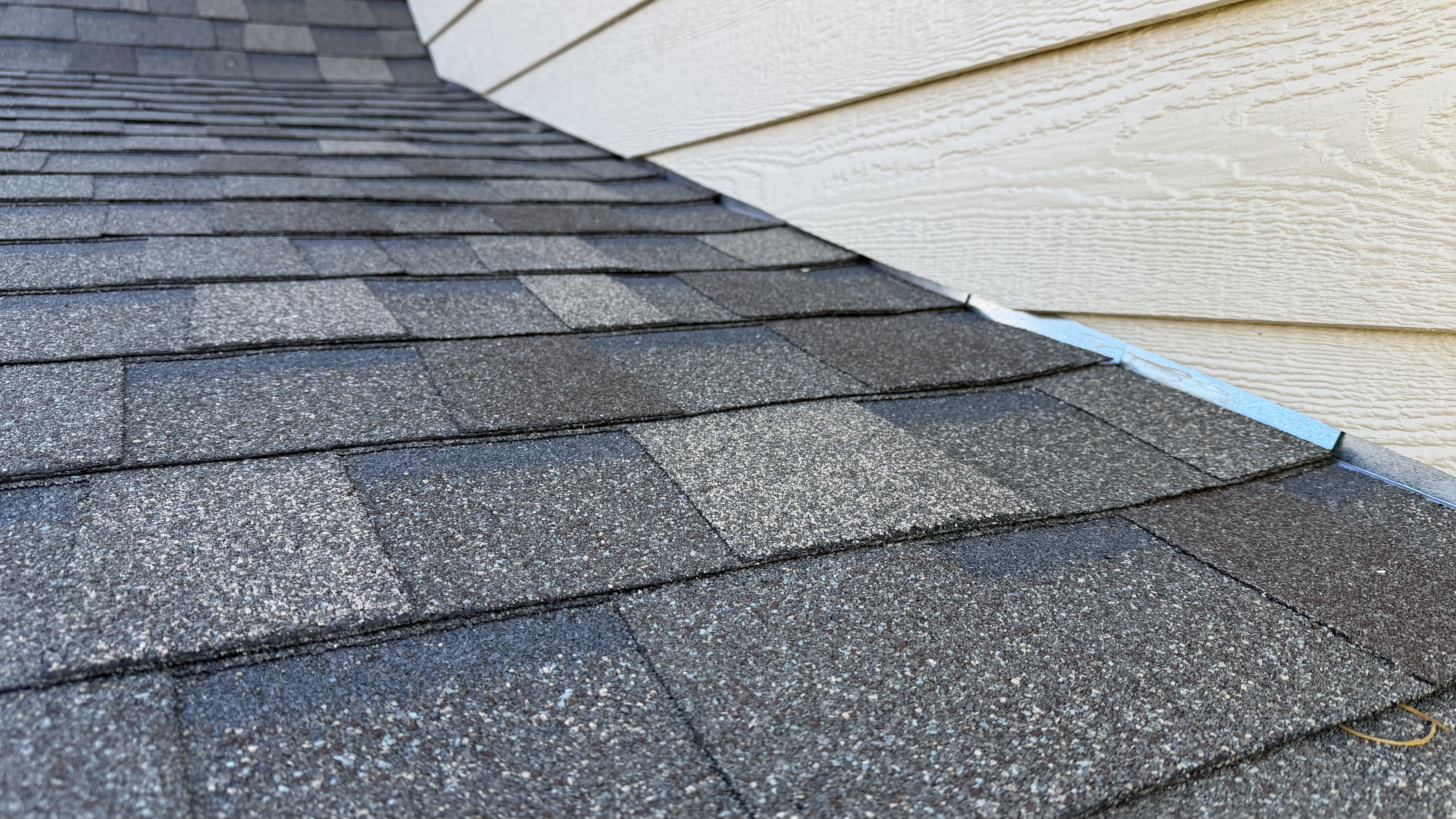 Clean sidewall flashing tucked perfectly under siding — drip edge visible at eave, every shingle course running dead straight back to ridge cap