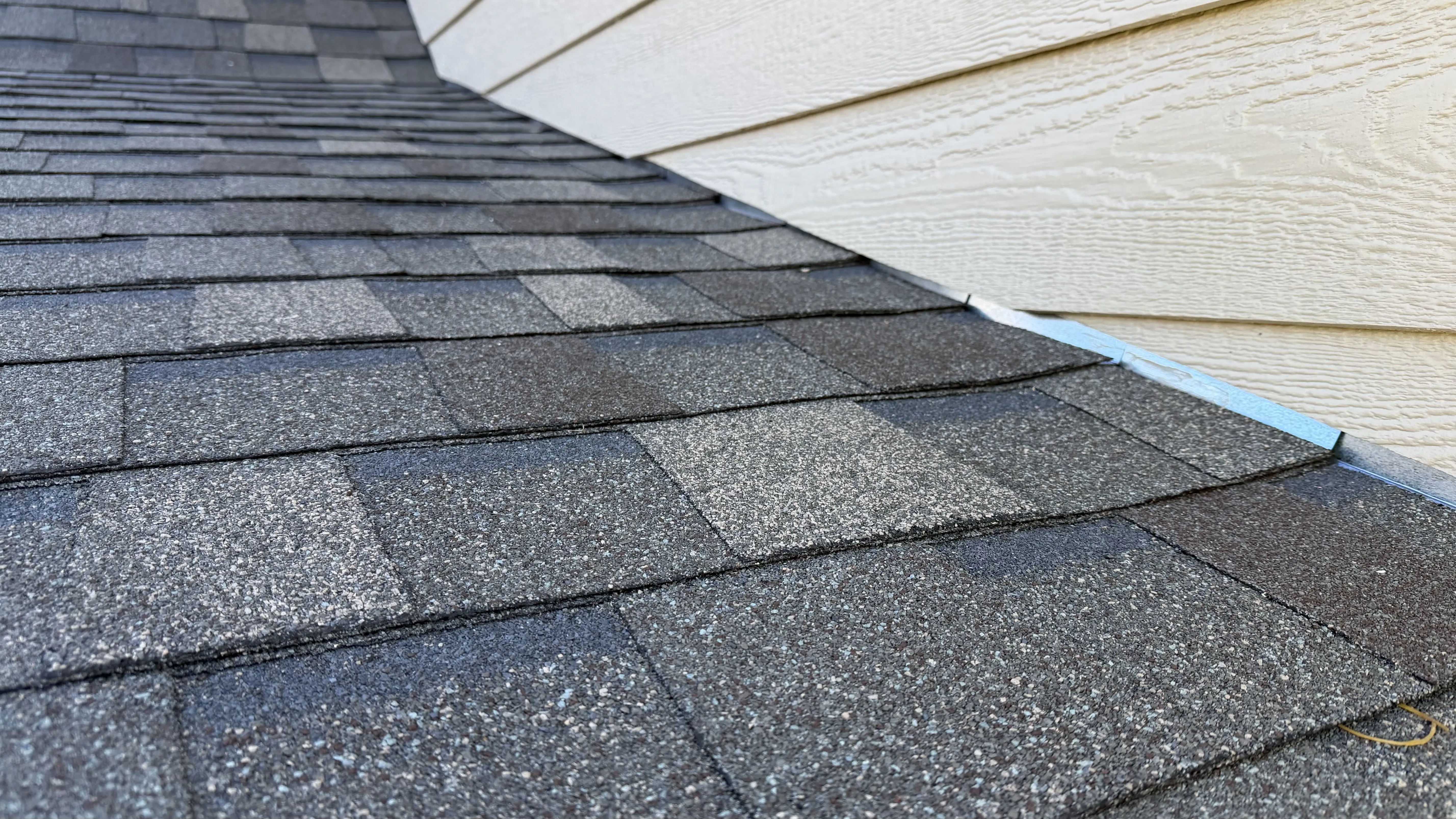 Clean sidewall flashing tucked perfectly under siding — drip edge visible at eave, every shingle course running dead straight back to ridge cap