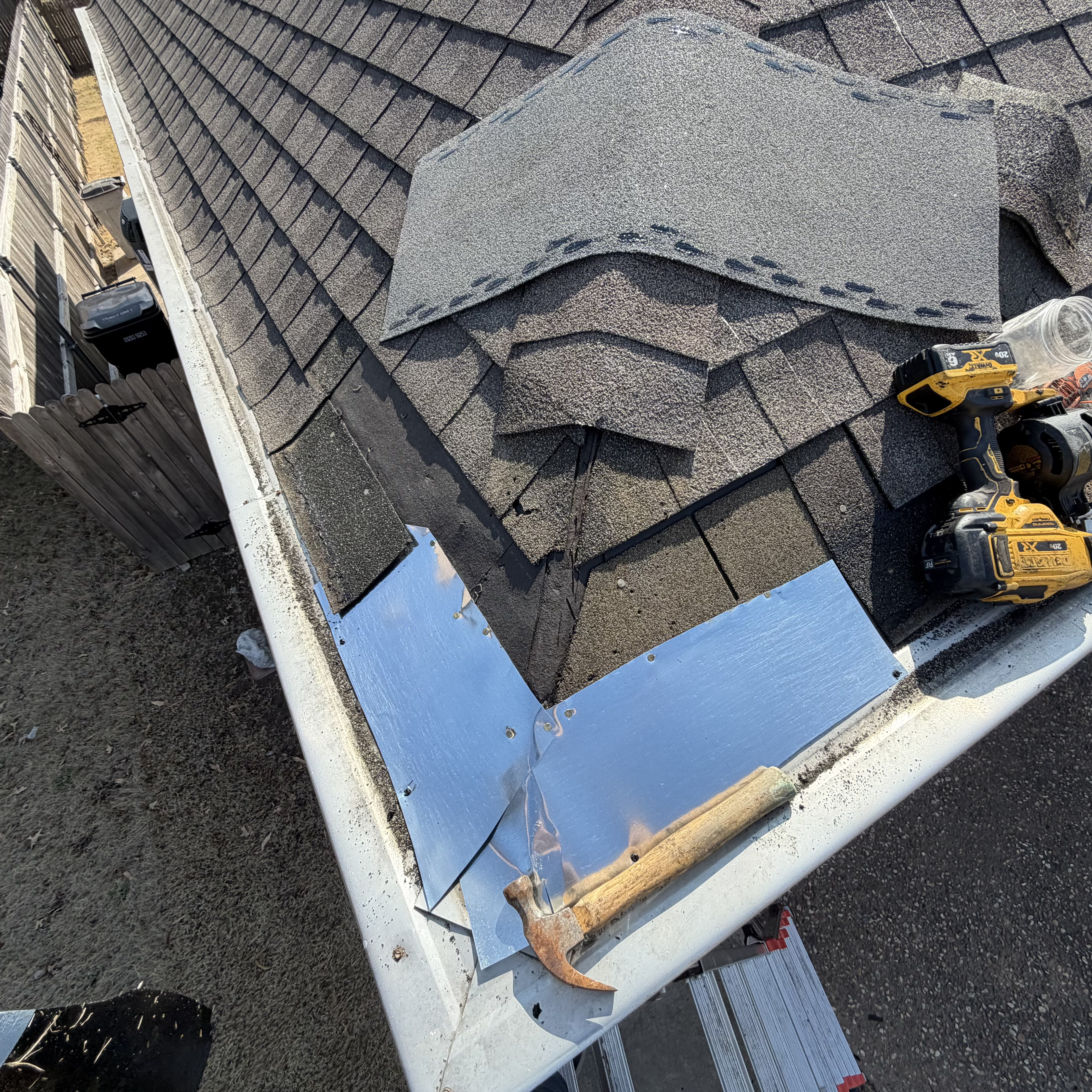 Eave repair in progress — shingles pulled back, new galvanized drip edge being installed, DeWalt drill and hammer in gutter, new shingles staged.