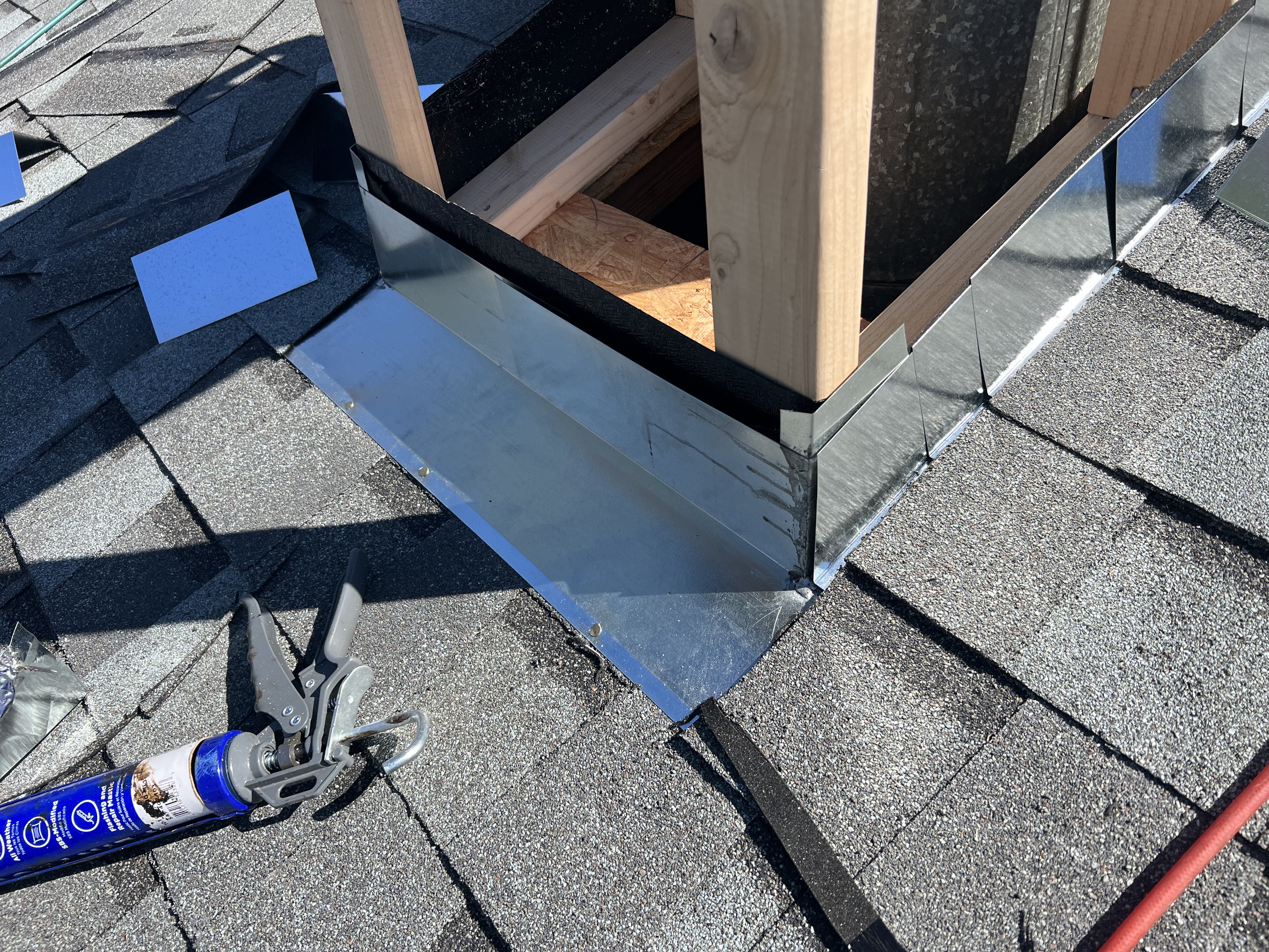 Custom galvanized curb flashing on skylight — step flashing tabs laid out, ice & water wrapped up curb framing, caulk gun on roof, red air hose