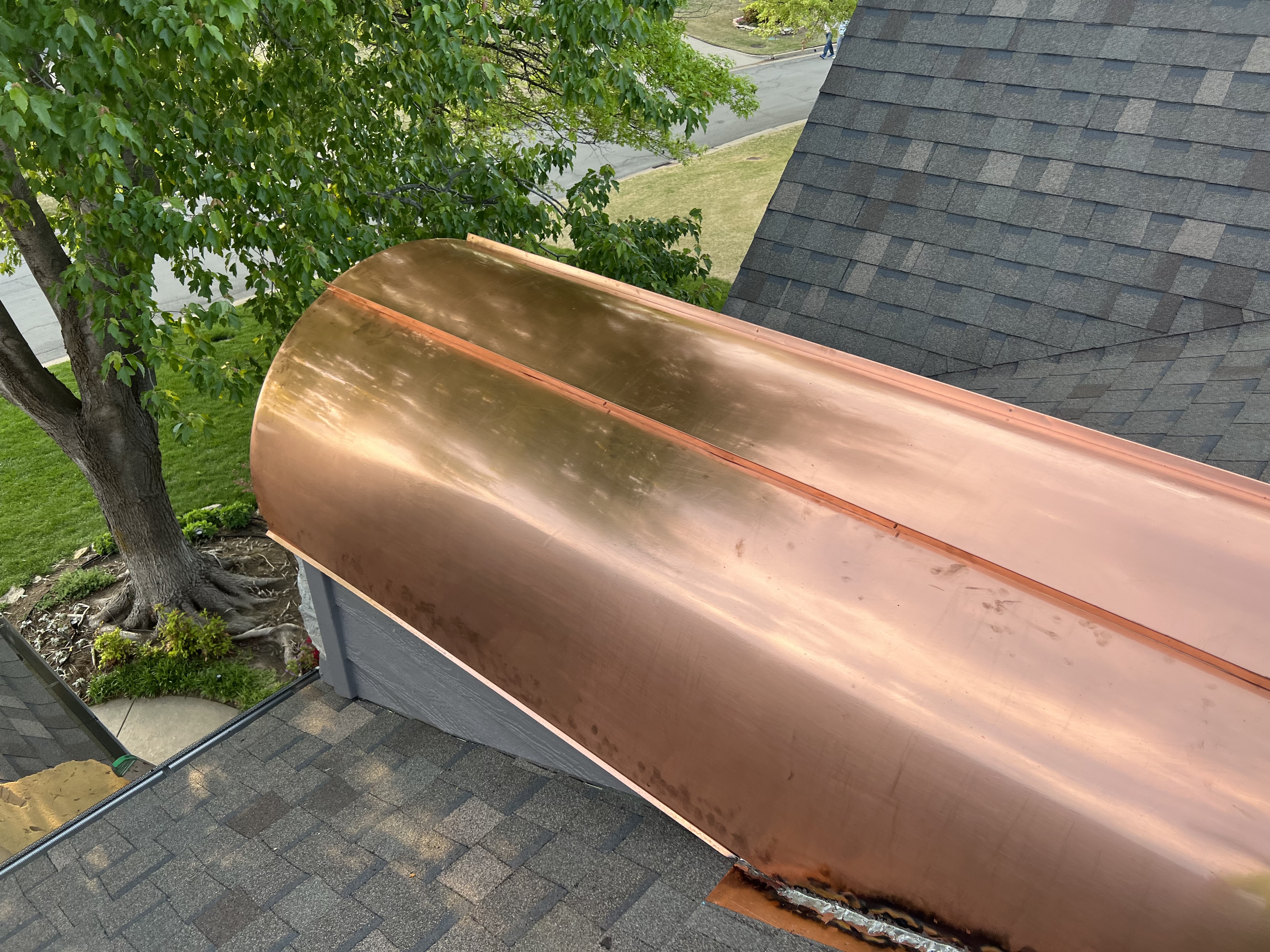 Copper eyebrow dormer — completed copper metal roof with gray shingle roof visible alongside in upper right. Shingle vs metal in one frame.