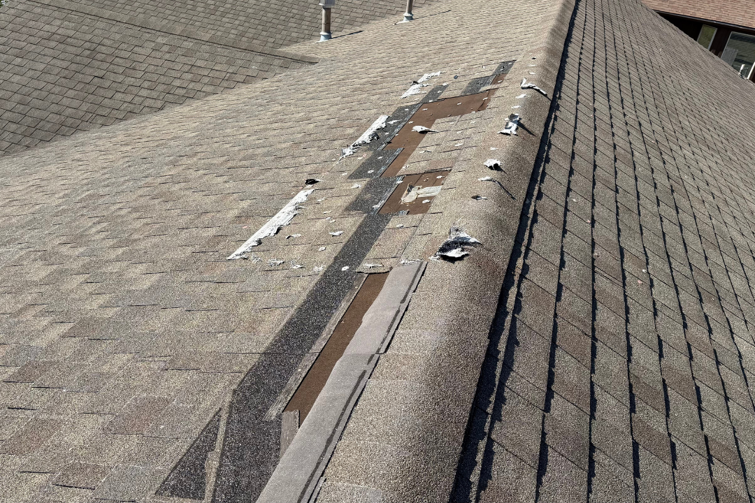 Ridge cap blown completely off — exposed decking, shingle debris scattered, Tulsa suburban neighborhood