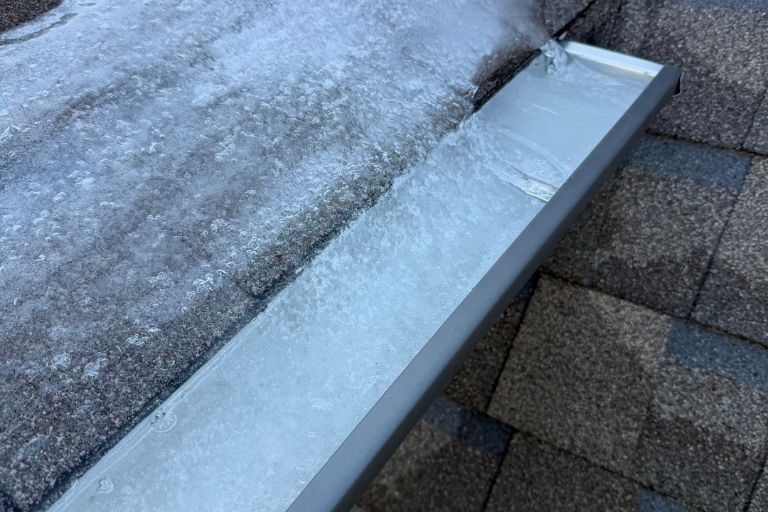 Ice dam frozen solid in gutter — ice backing up onto roof surface, shingles both sides