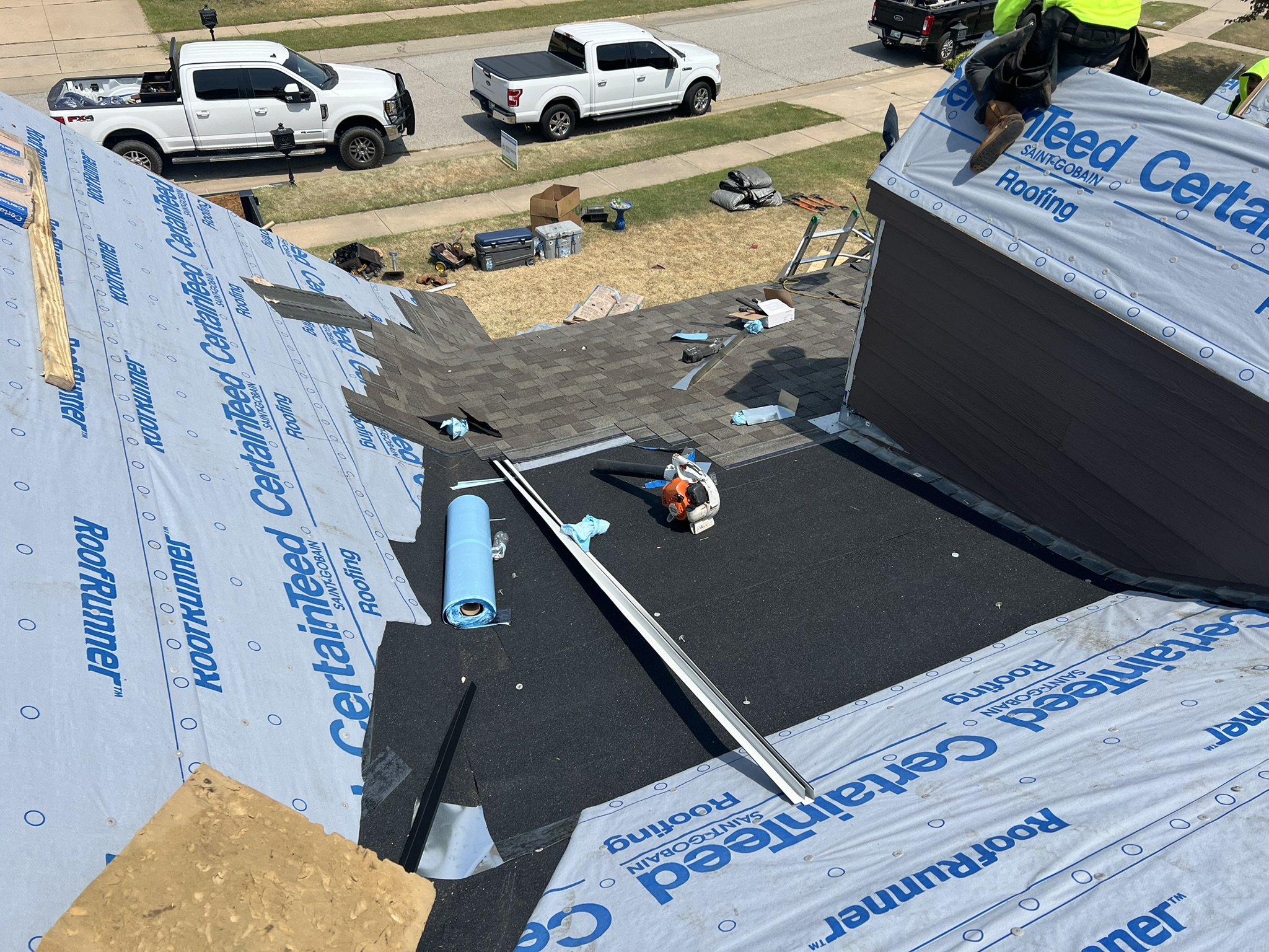 Aerial wide shot of full roof in progress with crew working and ice and water shield roll in valley