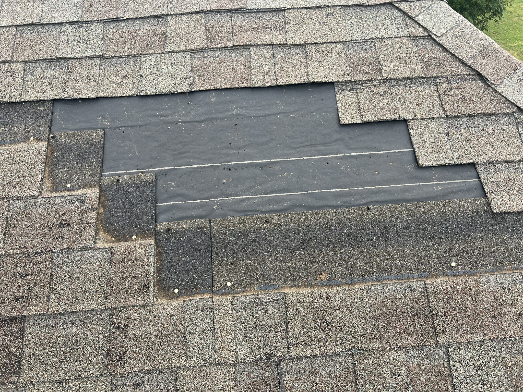 Localized repair in progress — underlayment exposed with clean cut lines around damaged section