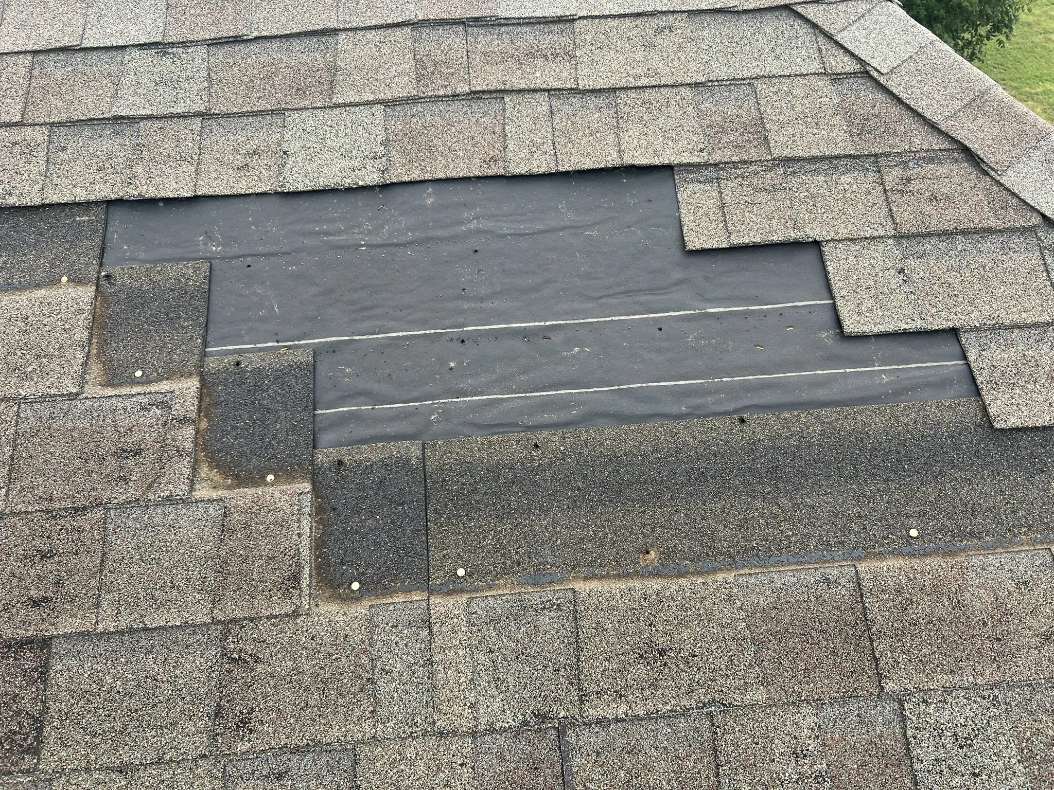 Localized repair in progress — underlayment exposed with clean cut lines around damaged section