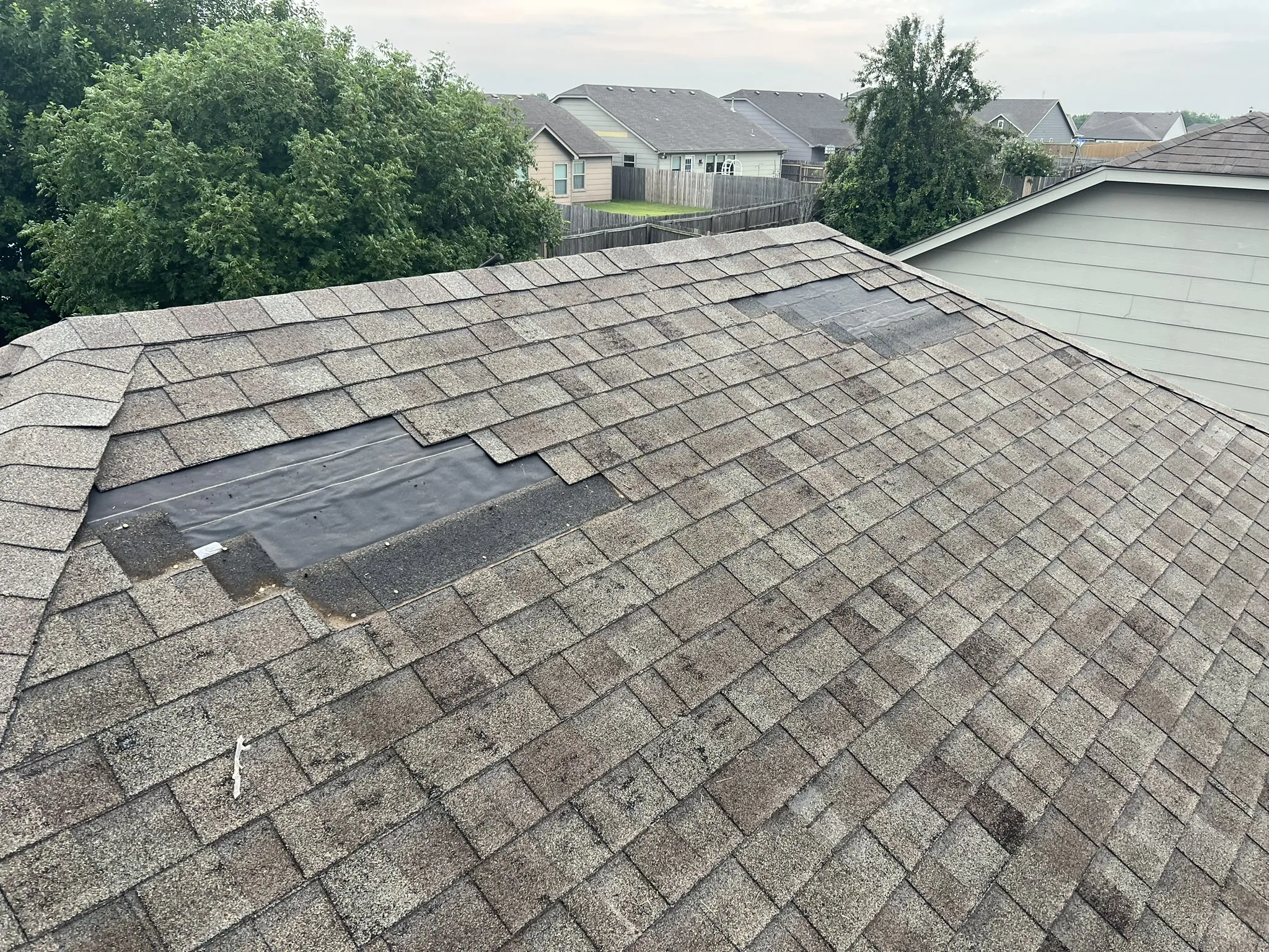 Blown shingles with exposed felt paper, wide shot of Tulsa neighborhood roof
