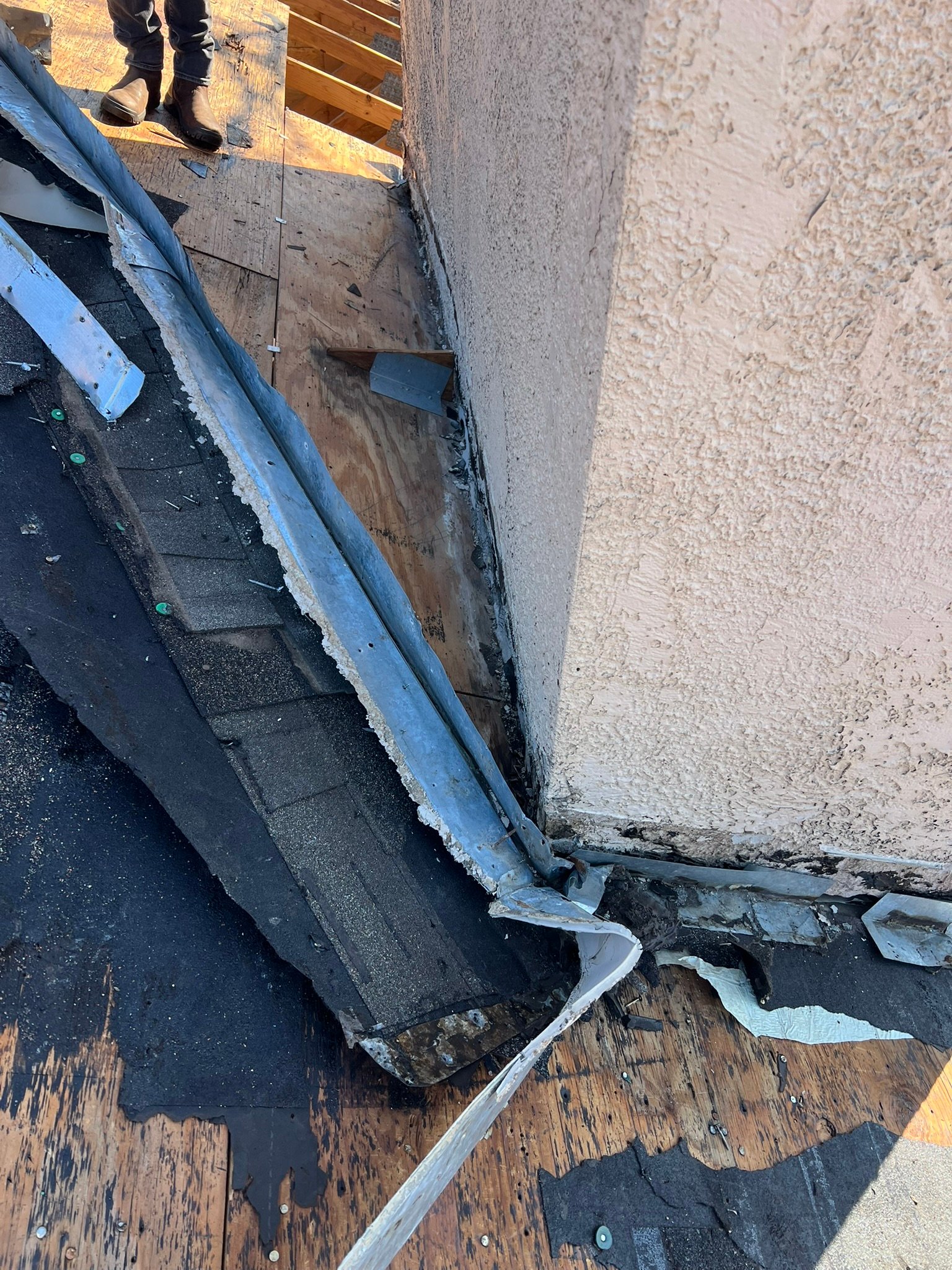 Failed wall flashing torn off with rotted deck exposed and stucco wall visible — higher-cost repair scope