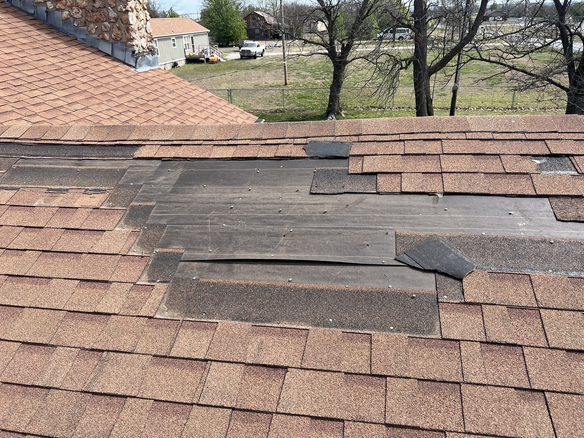 Wind damage wide shot showing blown shingles across Tulsa neighborhood roof