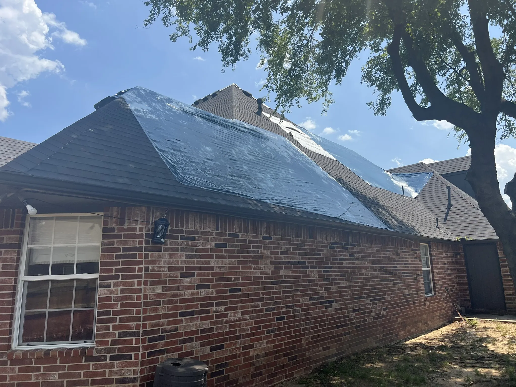 Ground level shot of brick home with blue tarp on failed roof, emergency situation