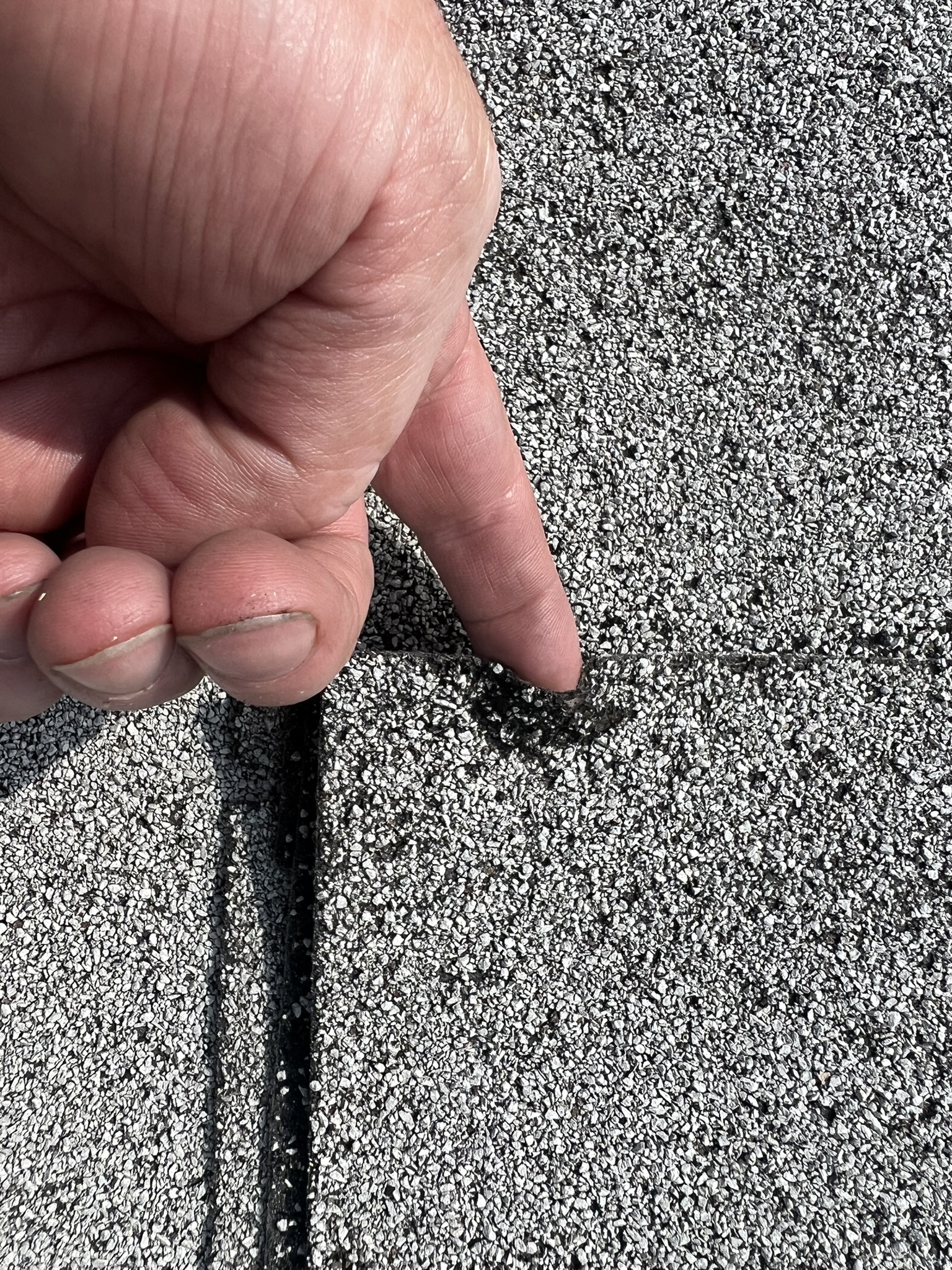 Finger pointing to hail cracked shingle on Tulsa roof