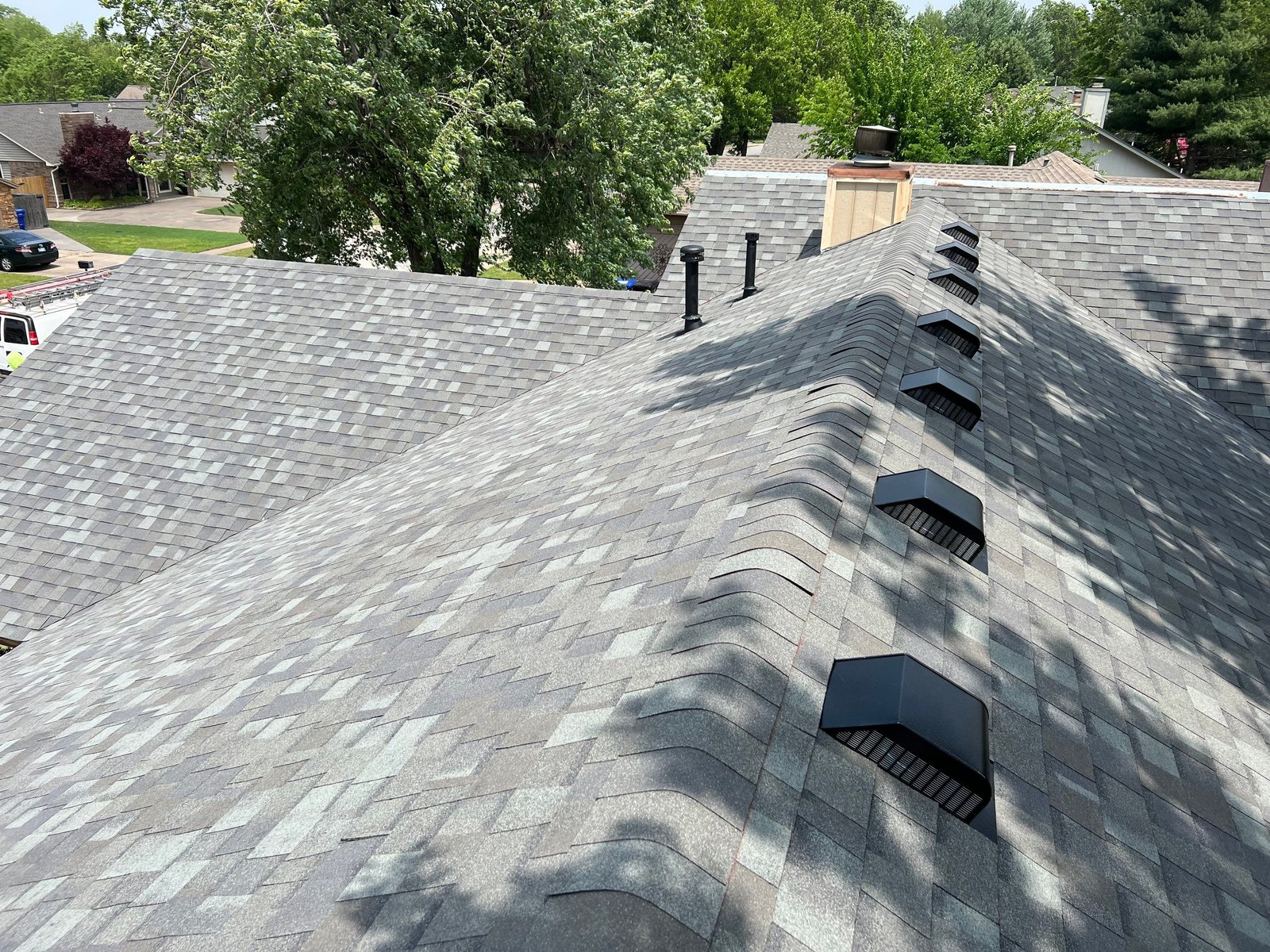 Row of 8 box vents along roof slope with two pipe stacks, green Tulsa neighborhood