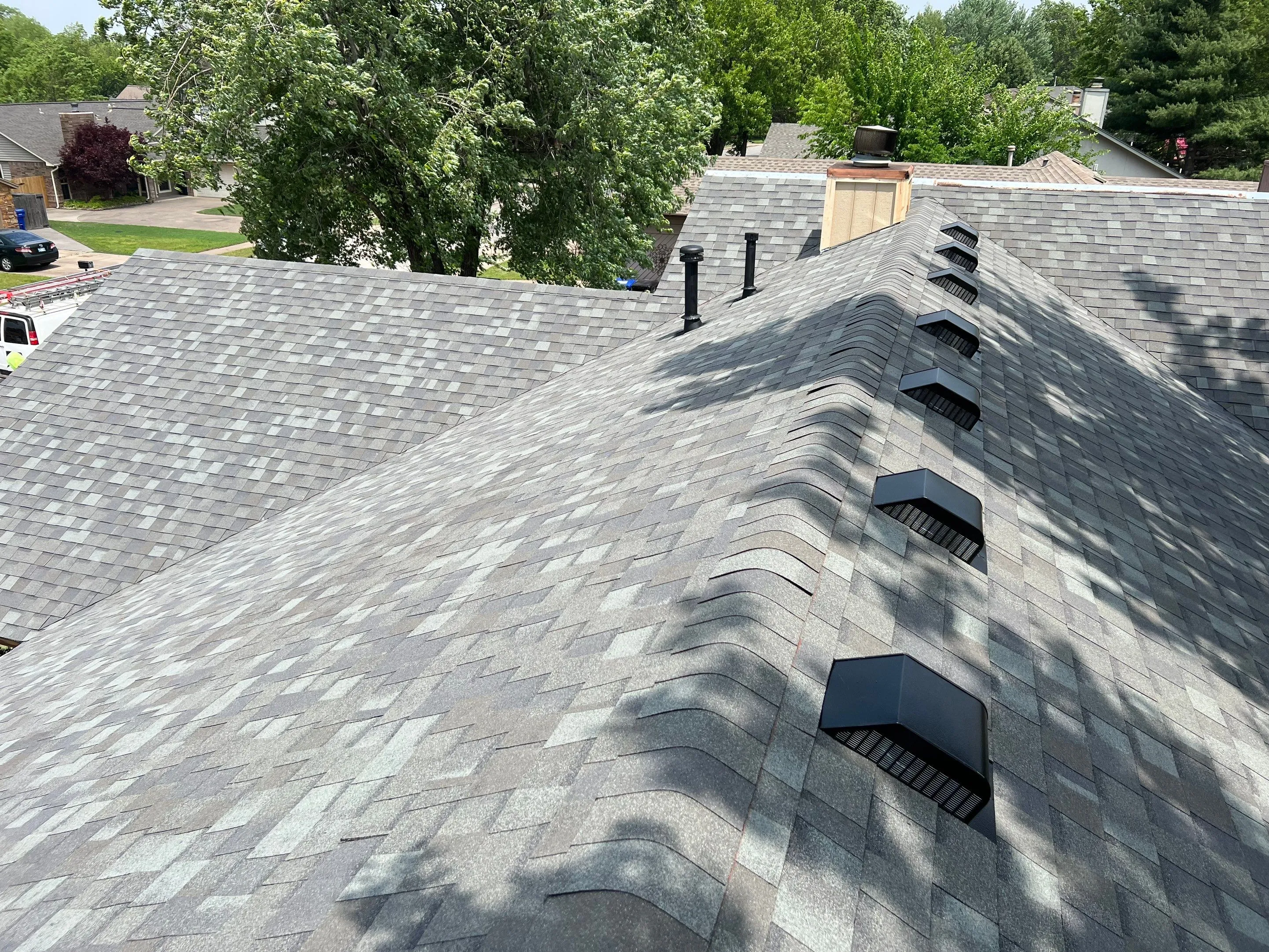 Row of 8 box vents along roof slope with two pipe stacks, green Tulsa neighborhood